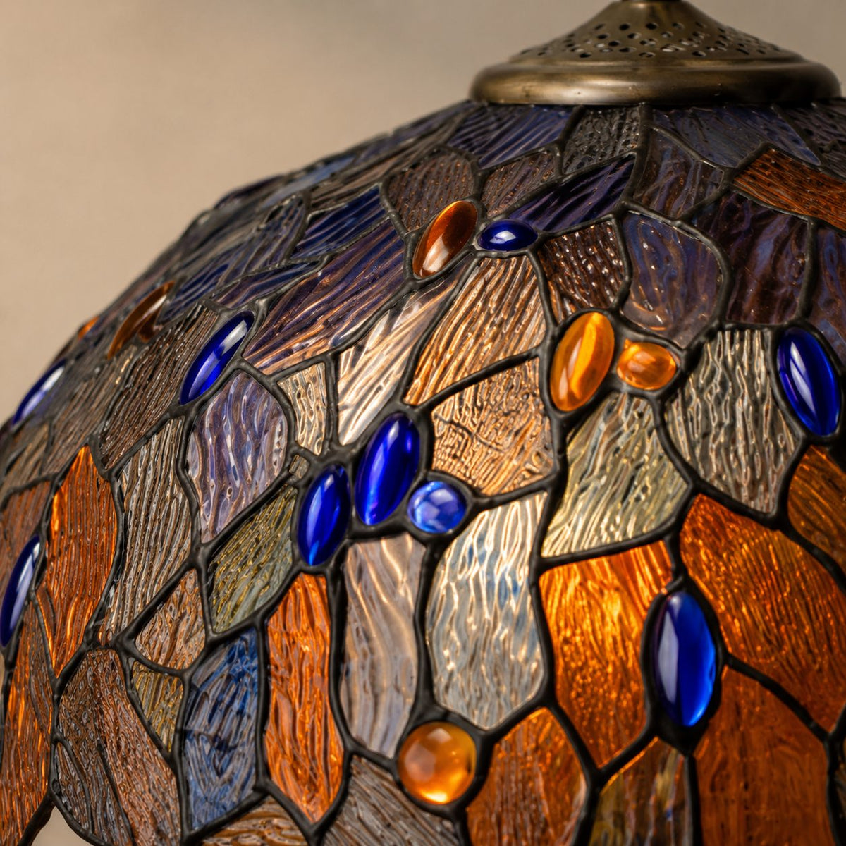 Lampe de style Tiffany à décor de feuillages bleus et ambrés, gros plan vitrail cabochons allumé