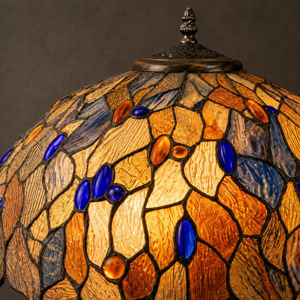 Lampe de style Tiffany à décor de feuillages bleus et ambrés, gros plan vitrail allumé fond sombre